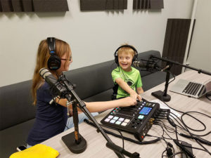 2 kids using the podcasting mixing board and microphones