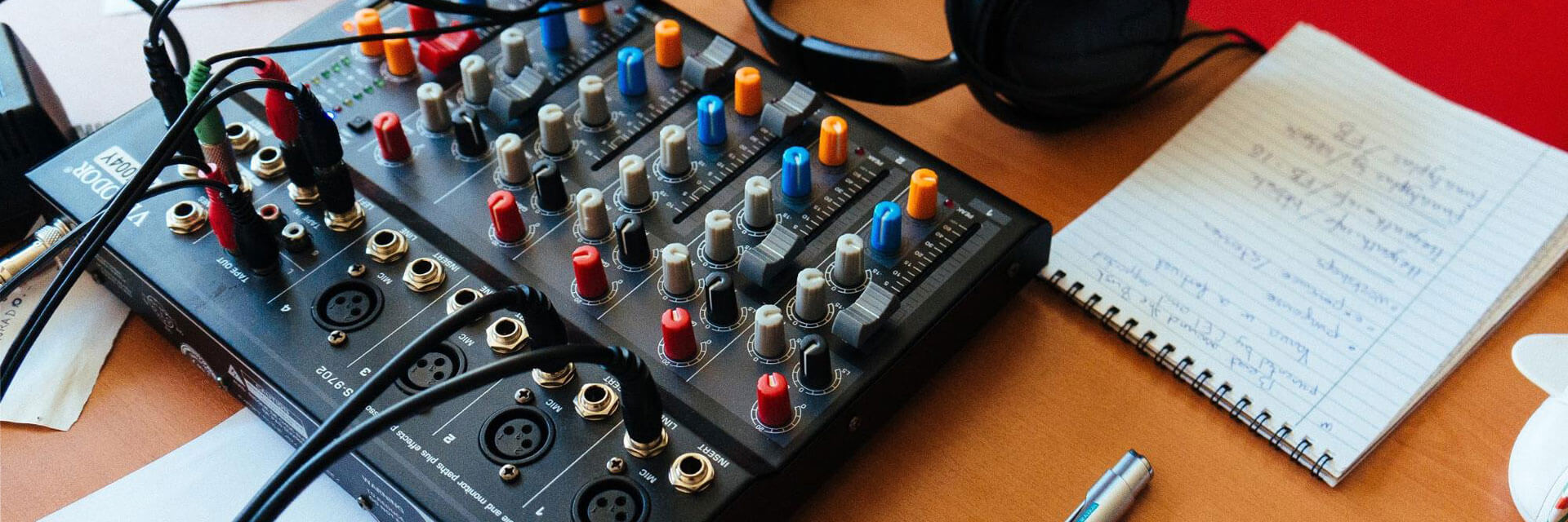 A table in a podcast studio with a notepad, mixing board and headphones